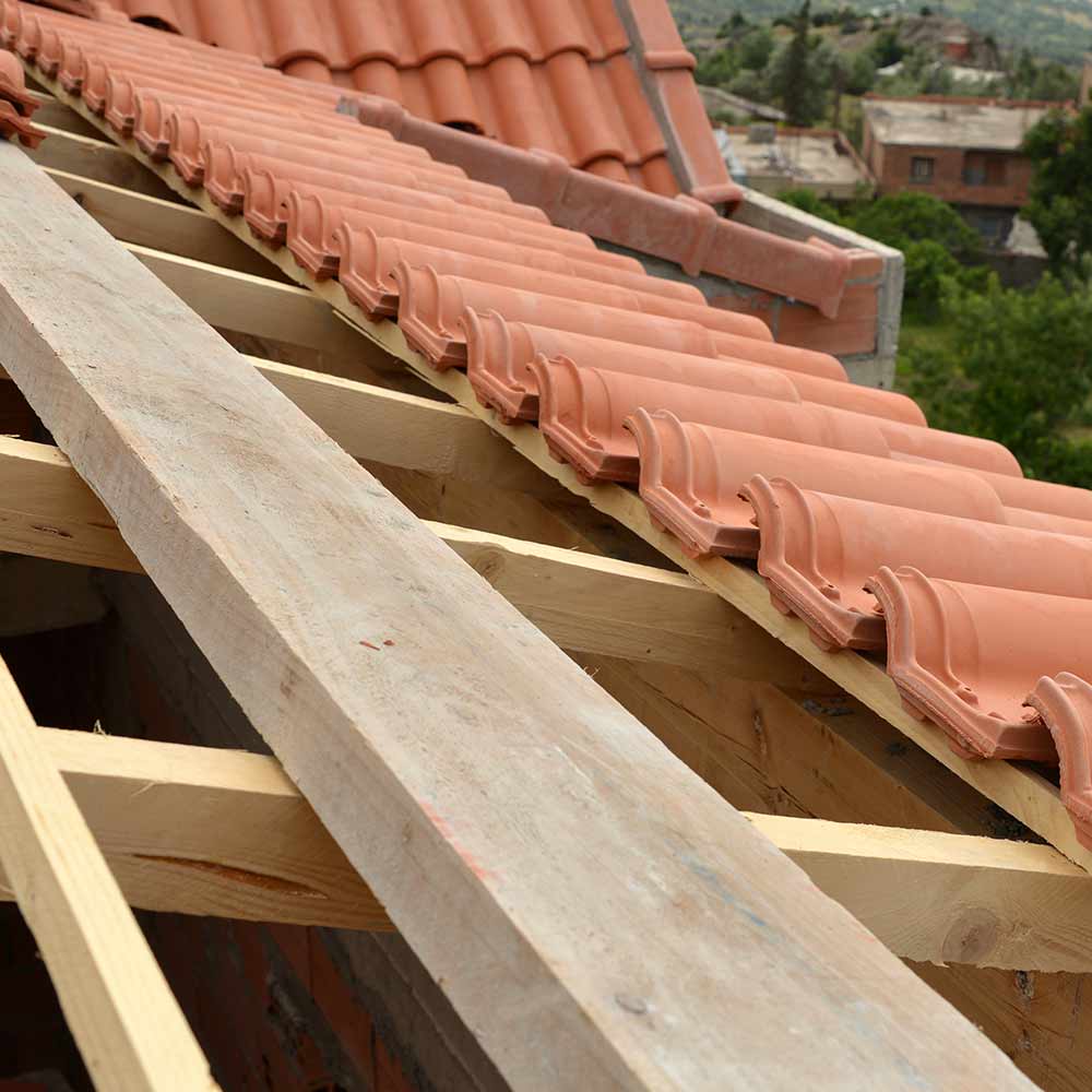 Construction de toiture en tuiles romanes oranges, montrant la charpente en bois claire et l'avancement de la pose des éléments.